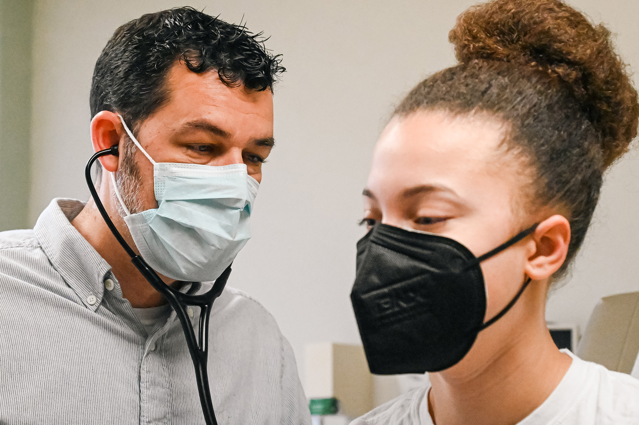 A medical provider with a stethoscope checks a student's breathing.