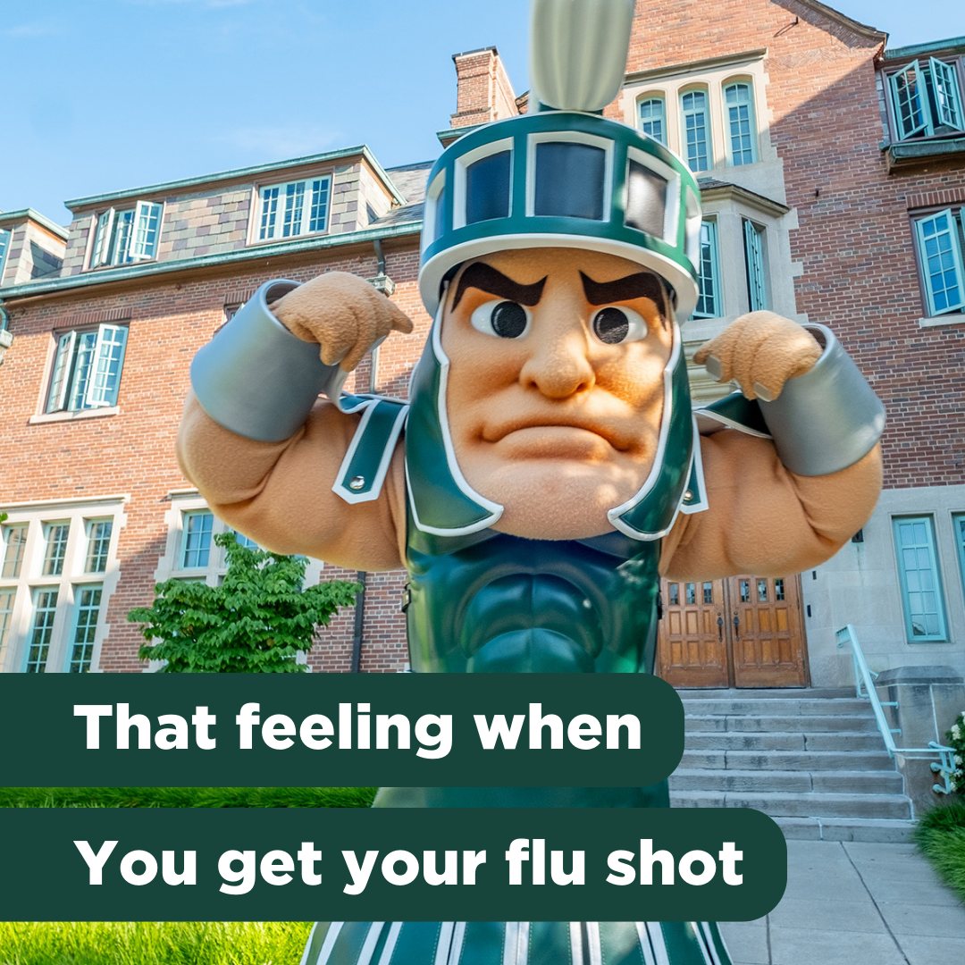 Sparty flexes his muscles in front of an older building on MSU's campus on a sunny day. Text reads, "that feeling when you get your flu shot"